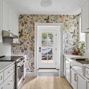 Narrow galley kitchen remodel with white cabinetry, floral wallpaper, and natural wood floors in Minneapolis.