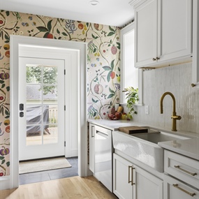Remodeled kitchen with white cabinets, brass fixtures, floral wallpaper, and a glass exterior door.