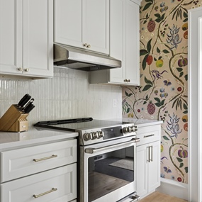 Stainless steel gas range with white shaker cabinets and floral wallpaper in a Minneapolis kitchen remodel.