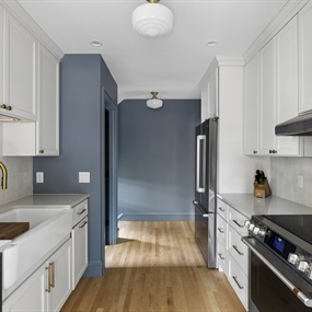 Full view of a remodeled galley kitchen with white cabinets, stainless steel appliances, and wood flooring.