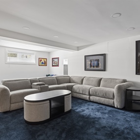 Remodeled basement family room with a large sectional sofa, ottoman, and built-in lighting in Minneapolis.