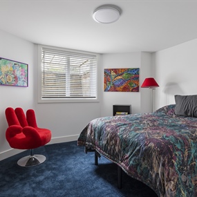 Finished basement bedroom with blue carpeting, a large bed, and a red accent chair in a Lynnhurst home.