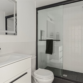 Remodeled basement bathroom featuring a white vanity, walk-in glass shower, and modern black fixtures.